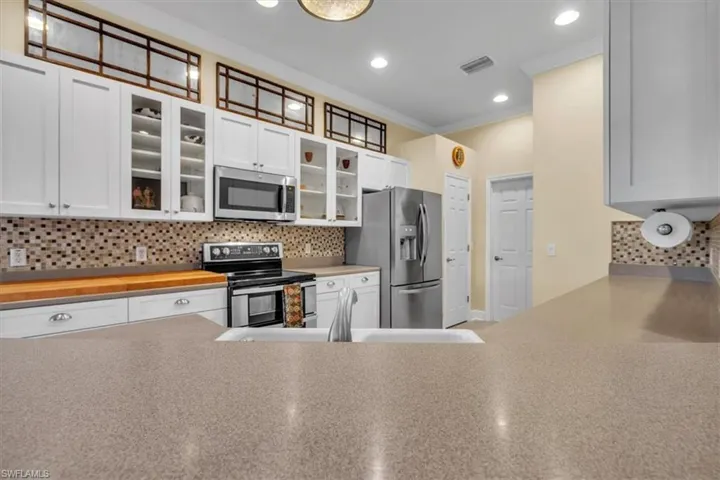 Kitchen featuring white cabinetry with glass-front uppers, transom windows, mosaic tile backsplash, solid-surface countertops, and stainless steel appliances
