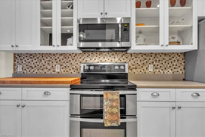 White cabinetry with glass-front upper doors, stainless steel dual-oven range, integrated microwave, and multi-tone mosaic tile backsplash