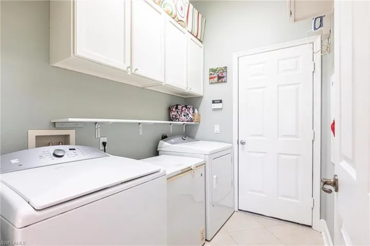 Laundry area featuring white shaker-style wall cabinetry, a white wall-mounted shelf, and neutral tile flooring