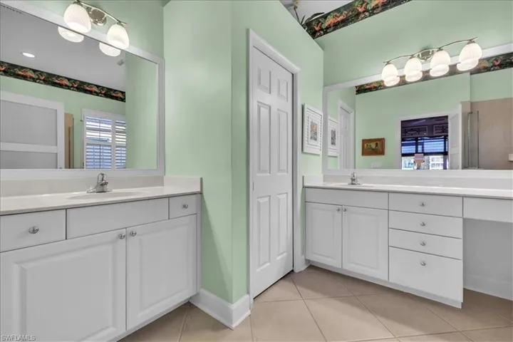 Dual white cabinetry vanities with stone countertops, oversized wall-to-wall vanity mirrors, integrated lighting fixtures, and tile flooring