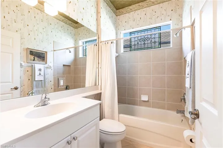 Bathroom featuring a vanity with a white countertop and oval sink, wall-spanning mirror, decorative leaded glass window, and tile-surround tub-shower combination