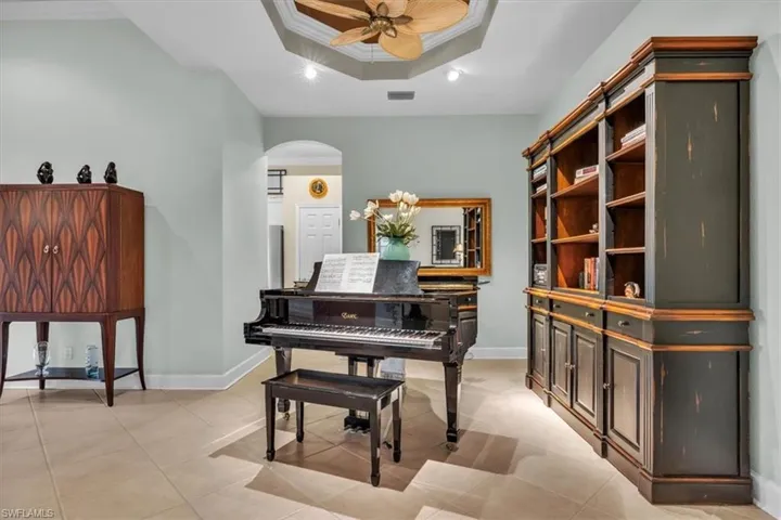 Custom built-in cabinetry with a dark finish, recessed tray ceiling, ceiling fan with palm-leaf blades, and neutral-toned tile flooring