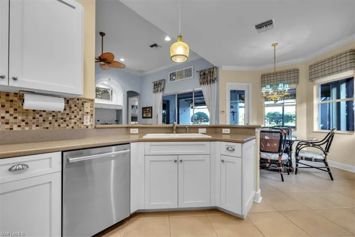 Kitchen featuring white cabinetry, solid-surface countertops, tile backsplash, stainless steel dishwasher, and ceramic tile flooring