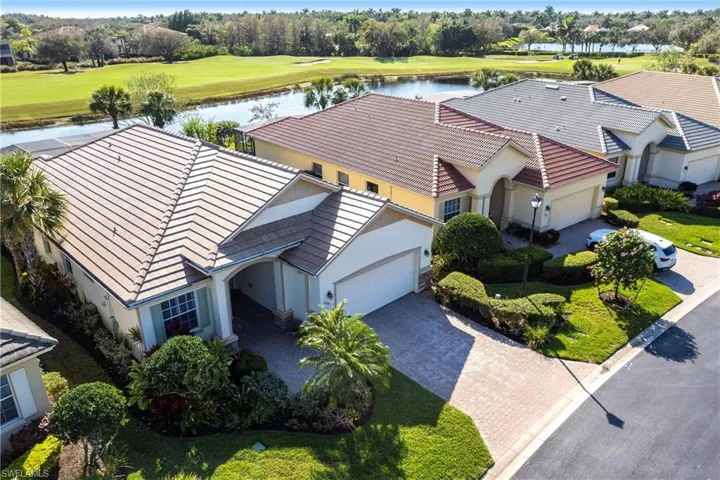 Stucco exterior featuring a multi-hipped tile roof, paver driveway, attached two-car garage, and landscaped grounds situated on a waterfront lot