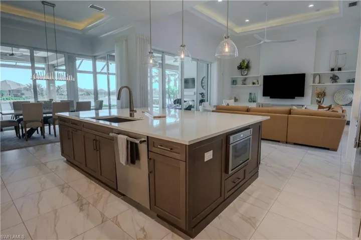 Kitchen featuring stainless steel dishwasher, a raised ceiling, ceiling fan, sink, and pendant lighting