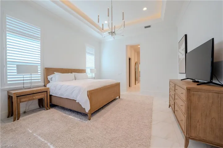 Bedroom with a raised ceiling, crown molding, and a notable chandelier
