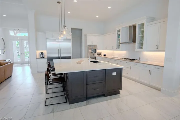 Kitchen with appliances with stainless steel finishes, wall chimney exhaust hood, a center island with sink, white cabinets, and hanging light fixtures