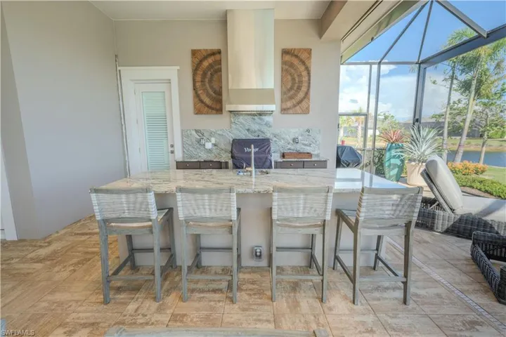 Kitchen with wall chimney exhaust hood, black range with electric cooktop, tasteful backsplash, light stone counters, and a breakfast bar area