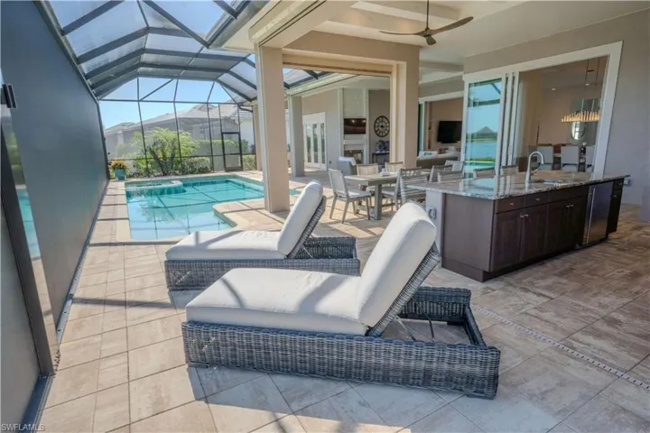 View of pool with glass enclosure, ceiling fan, a patio area, and a wet bar