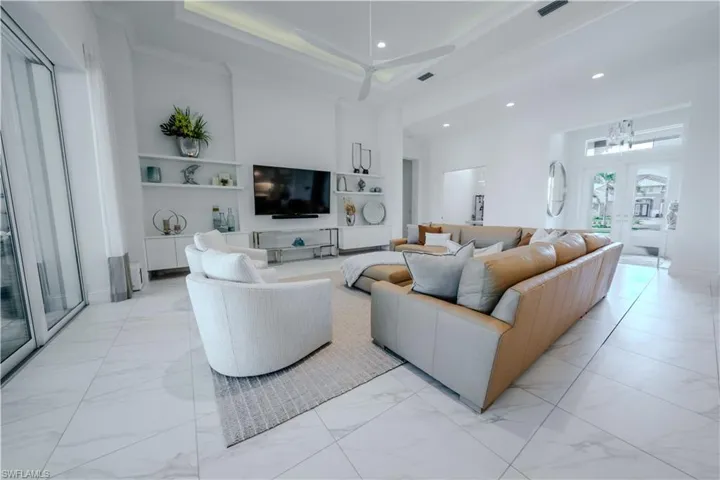Living room featuring a towering ceiling, built in shelves, a tray ceiling, crown molding, and a chandelier
