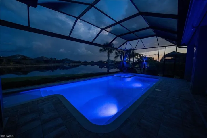 Pool at dusk with a jacuzzi, a patio, and a lanai