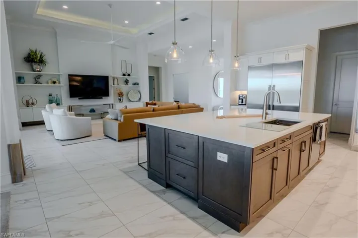 Kitchen with pendant lighting, sink, an island with sink, a tray ceiling, and stainless steel built in refrigerator