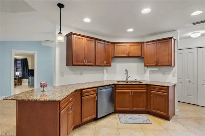 Kitchen featuring light tile patterned floors, stainless steel dishwasher, light stone countertops, decorative light fixtures, and sink