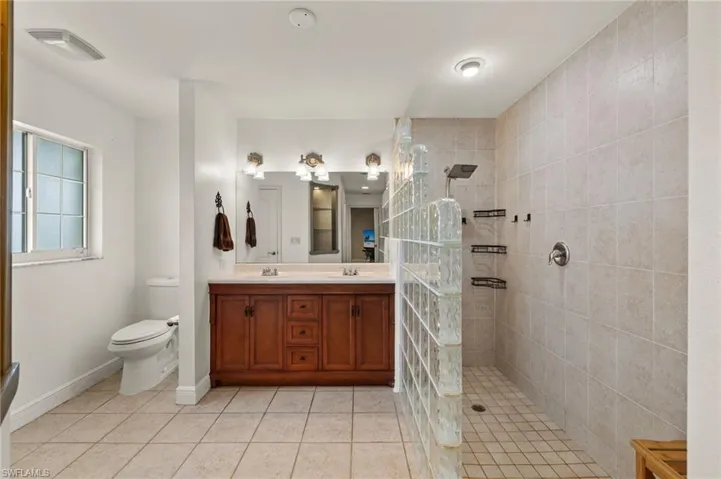 Bathroom with tile patterned flooring, dual vanity, toilet, and a tile shower