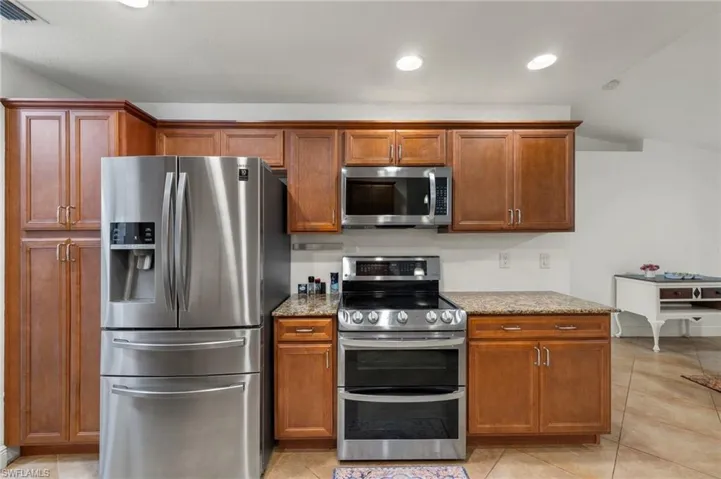 Kitchen with appliances with stainless steel finishes, light stone counters, and light tile patterned floors