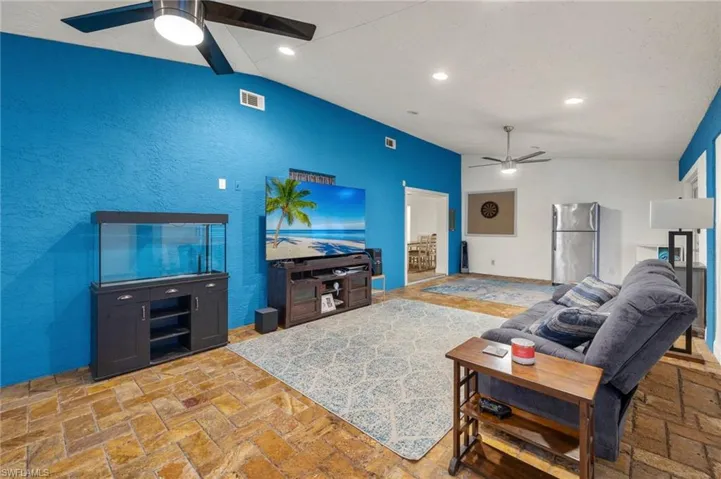 Living room with light tile patterned floors, ceiling fan, and vaulted ceiling with beams