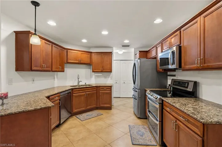 Kitchen with dark stone countertops, light tile patterned floors, hanging light fixtures, appliances with stainless steel finishes, and sink