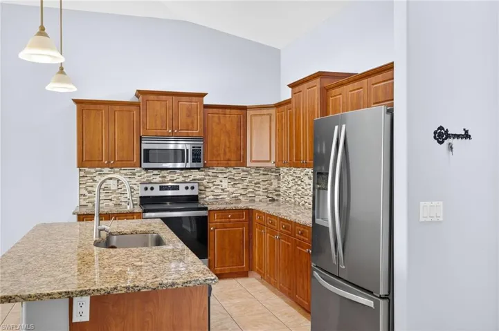 Kitchen with stainless steel appliances, tasteful backsplash, vaulted ceiling, an island with sink, and light tile patterned flooring