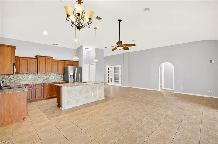 Kitchen with brown cabinetry, a ceiling fan, tasteful backsplash, light tile patterned floors, and light stone countertops