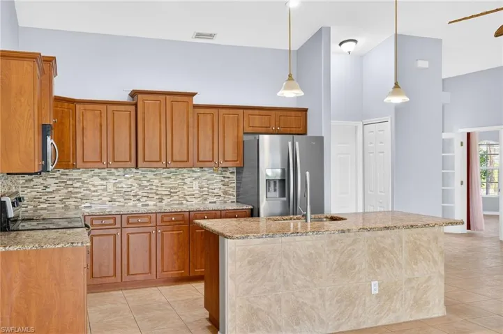 Kitchen featuring appliances with stainless steel finishes, decorative backsplash, light stone counters, brown cabinetry, and a towering ceiling