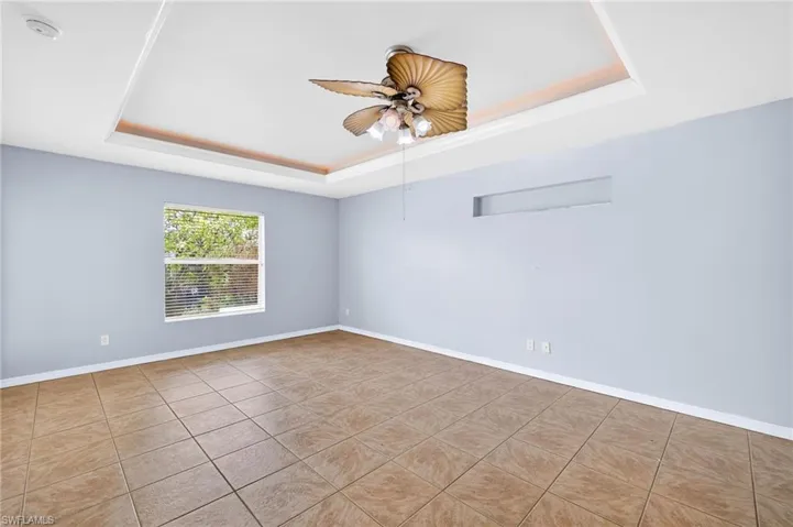 Tiled empty room featuring a raised ceiling and a ceiling fan