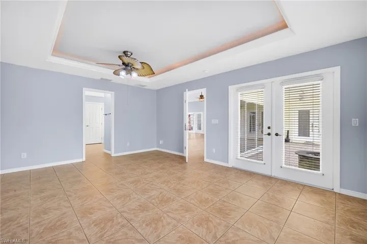 Empty room with a tray ceiling, french doors, light tile patterned flooring, and ceiling fan