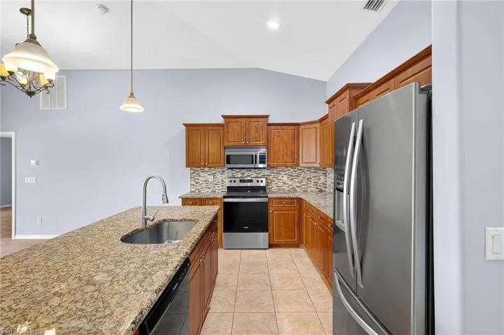 Kitchen with stainless steel appliances, brown cabinets, tasteful backsplash, light tile patterned flooring, and lofted ceiling