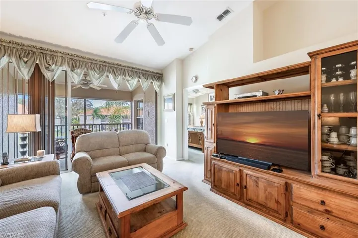 Living room with light carpet, a towering ceiling, visible vents, and a ceiling fan