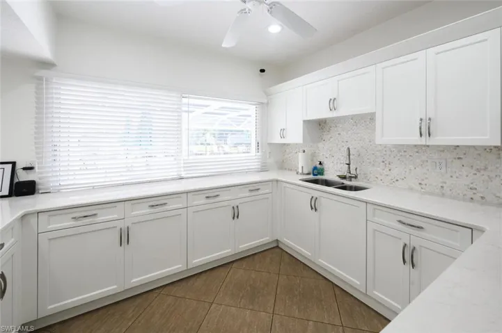 Kitchen with a ceiling fan, a sink, tile patterned flooring, white cabinetry, and backsplash