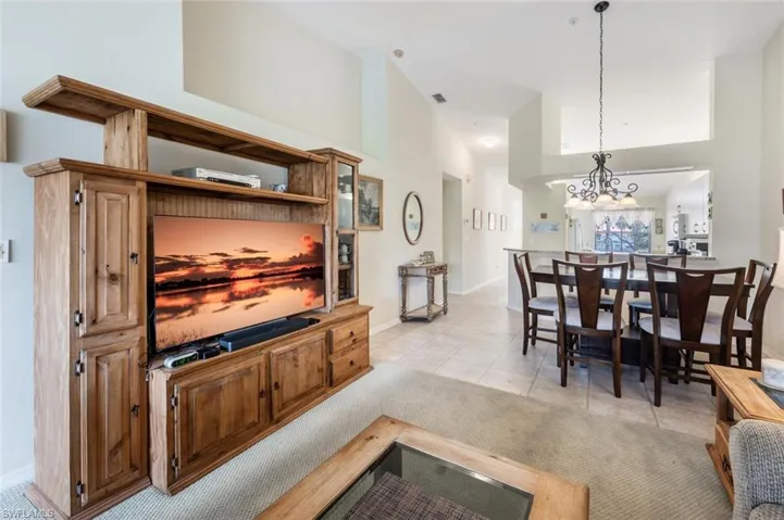 Living area featuring a notable chandelier, light tile patterned floors, visible vents, a high ceiling, and baseboards