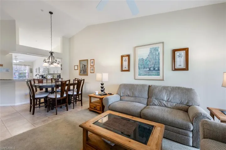 Living room with lofted ceiling, light tile patterned floors, baseboards, and ceiling fan with notable chandelier
