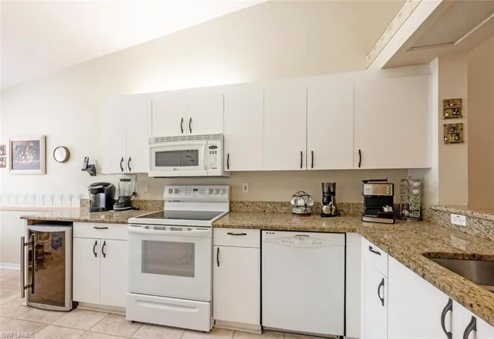 Kitchen featuring beverage cooler, white appliances, light stone counters, and white cabinets