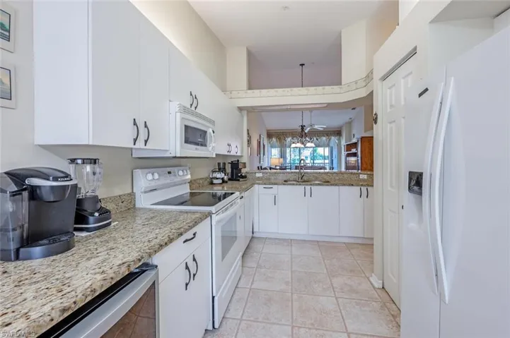 Kitchen with light tile patterned floors, white appliances, a sink, white cabinetry, and light stone countertops