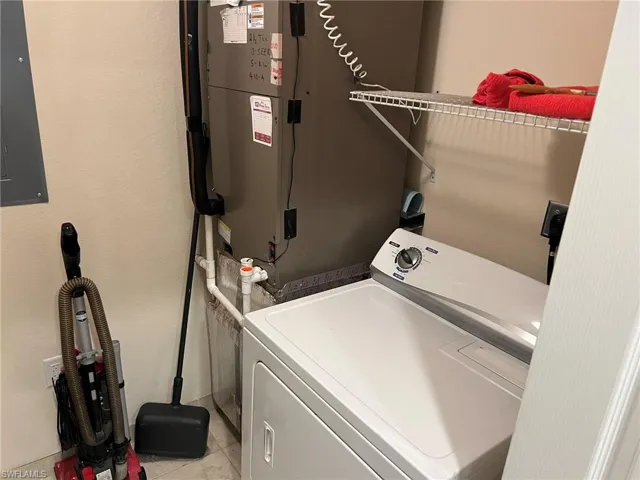 Clothes washing area with laundry area, light tile patterned floors, electric panel, and washer / dryer
