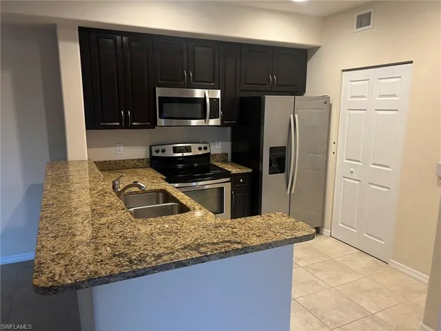 Kitchen featuring a peninsula, visible vents, dark cabinetry, stainless steel appliances, and a sink