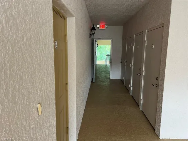 Corridor with a textured ceiling, a textured wall, and carpet floors