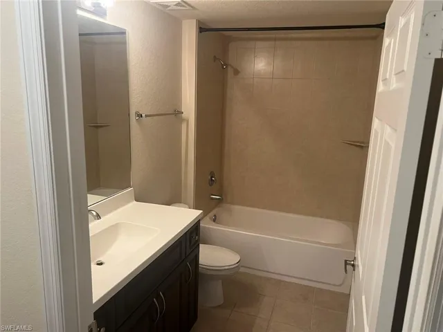 Full bathroom featuring a textured wall, tile patterned floors, vanity, and toilet