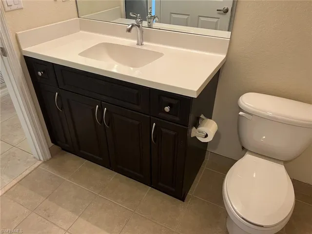Half bath featuring toilet, vanity, and a textured wall