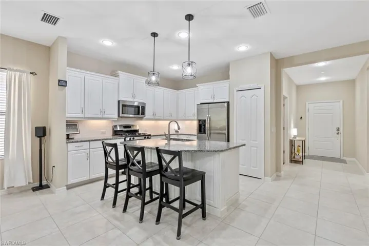 Kitchen featuring appliances with stainless steel finishes, sink, dark stone countertops, white cabinets, and a center island with sink