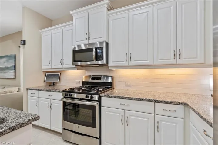 Kitchen with light tile patterned flooring, stainless steel appliances, decorative backsplash, and white cabinets