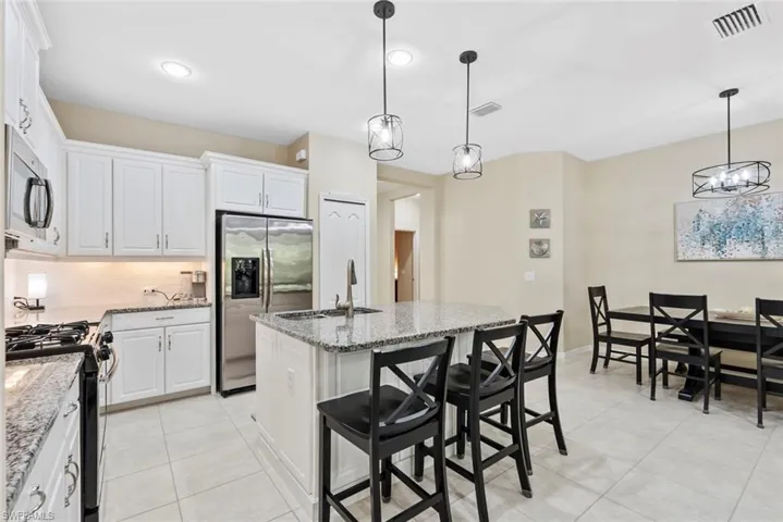 Kitchen featuring light stone counters, pendant lighting, stainless steel appliances, a kitchen island with sink, and white cabinets