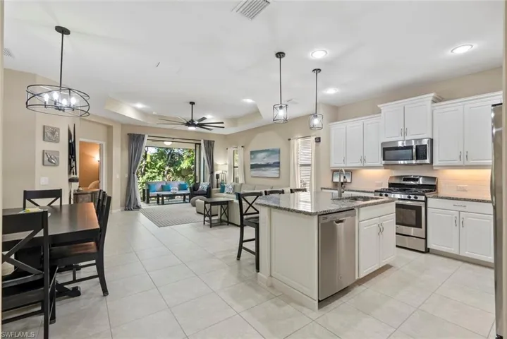 Kitchen featuring appliances with stainless steel finishes, white cabinets, hanging light fixtures, a kitchen island with sink, and light stone counters
