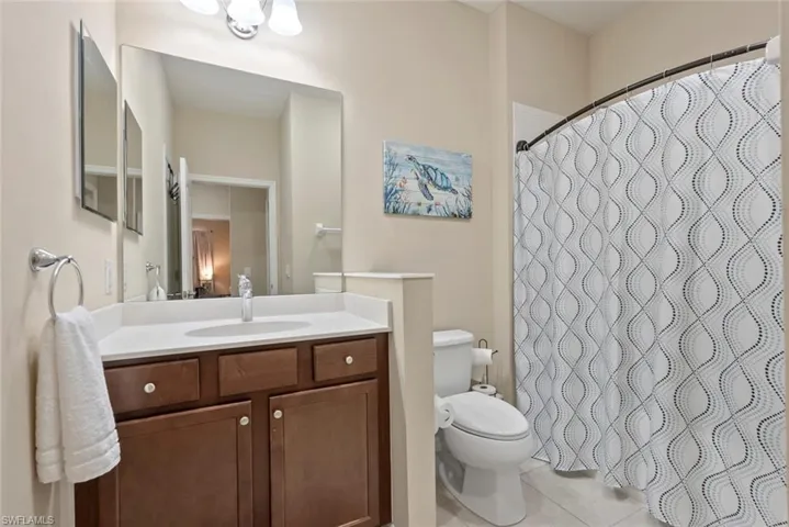 Bathroom with vanity, curtained shower, tile patterned floors, and toilet