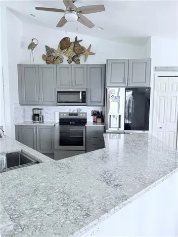 Kitchen with gray cabinets, stainless steel appliances, light stone counters, lofted ceiling, and decorative backsplash