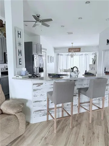 Kitchen with light stone countertops, gray cabinetry, a kitchen bar, and light wood-type flooring