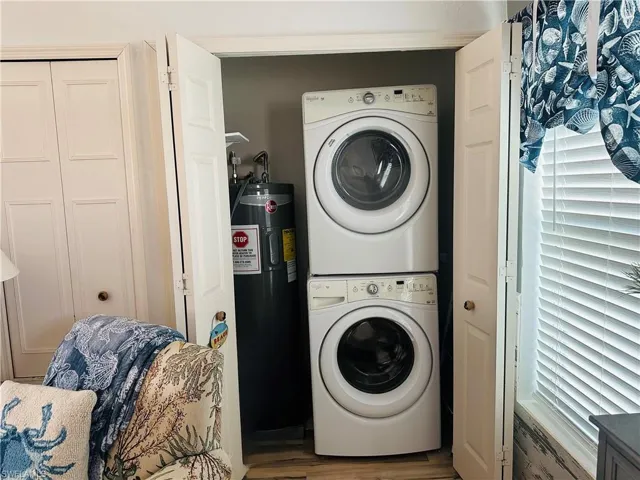 Washroom featuring stacked washer / dryer, wood finished floors, and electric water heater