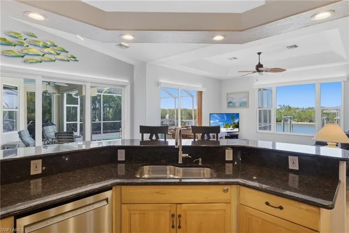 Kitchen featuring open floor plan, a raised ceiling, a sunroom, dark stone counters, and healthy amount of natural light