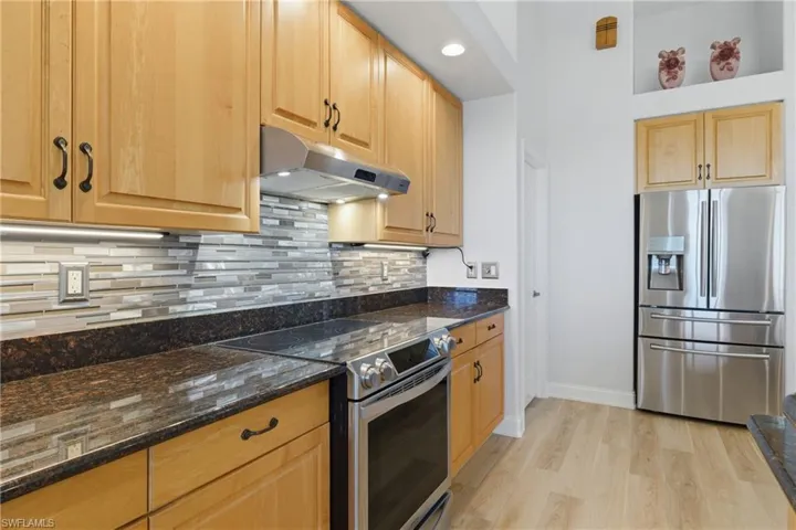 Kitchen with stainless steel appliances, dark stone countertops, light wood-style flooring, light wood finish cabinets, and recessed lighting