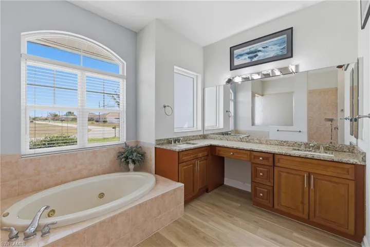 Bathroom featuring double vanity, a tub with jets, light wood-style floors, and tiled shower