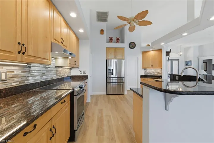 Kitchen with recessed lighting, stainless steel appliances, dark stone countertops, light wood-type flooring, and tasteful backsplash